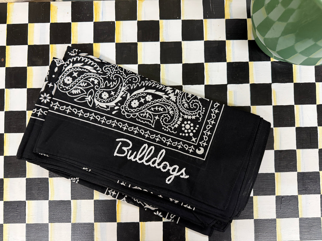 A black bandana-style cloth with white paisley print and the word 'Bullocks' in script, laid flat on a black-and-white checkered surface.